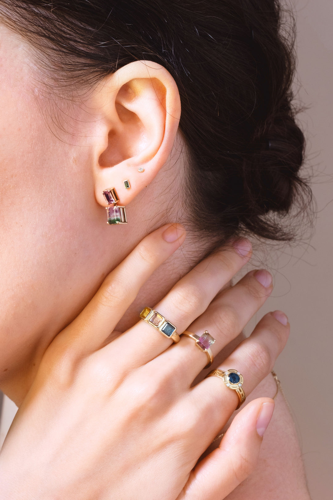 close up of a womans hand wearing lots of rings including watermelon sugar and golden futures rings. Also close up of wearing an earring stack
