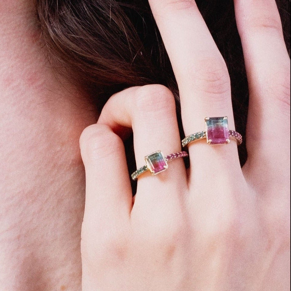 Close-up of a woman wearing a gold necklace and multicolored ring on a neutral background