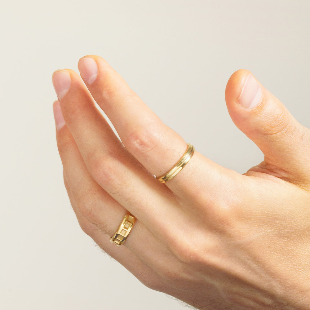 mans hand wearing two solid yellow gold male engagement rings