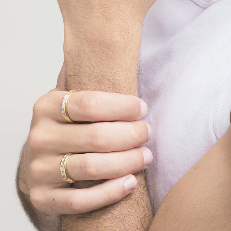two yellow gold mens engagement rings worn on mans hand holding onto other wrist