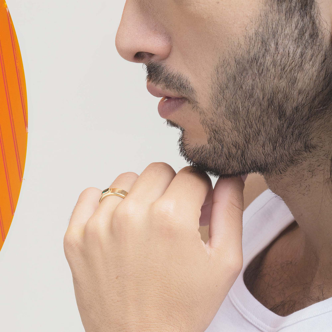 close up of a man with his fist to his chin wearing a yellow gold mens engagement ring set with a green emerald