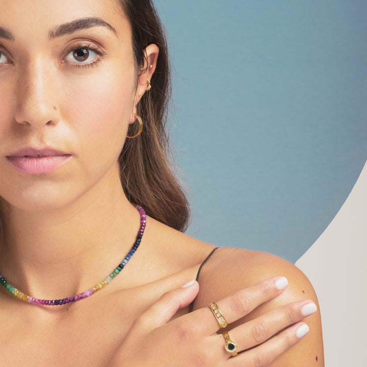 close up of woman wearing yellow gold hoop earrings and rainbow sapphire necklace and yellow gold rings