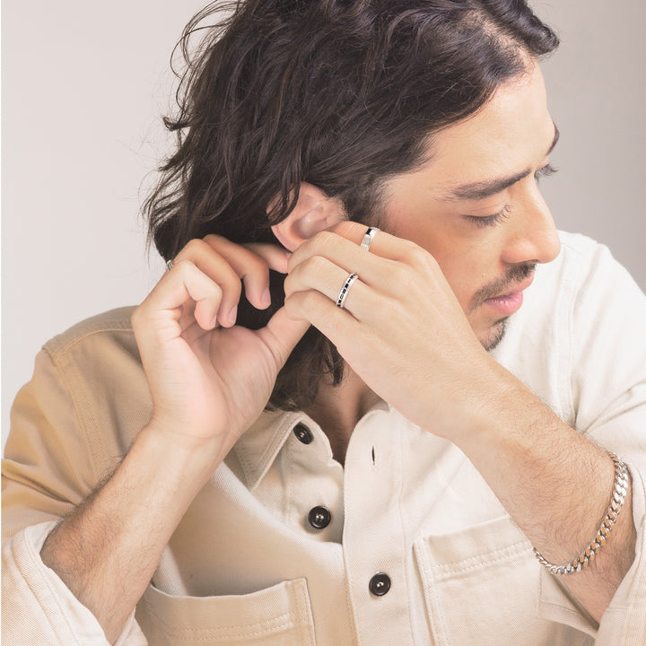 close up of man wearing a set of white gold rings and a silver chain bracelet adjusting his earrings and wearing a white shirt
