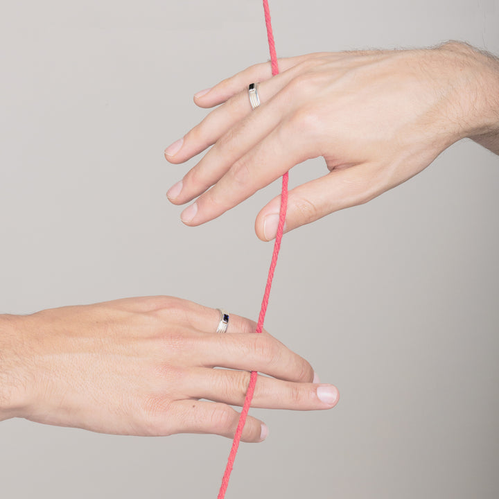 two mans hands wearing white gold engagement rings and holding onto the same red string