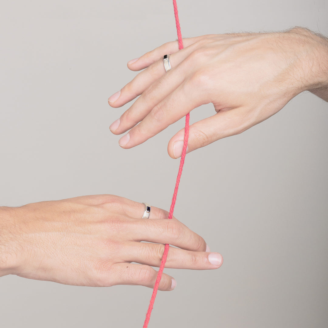 two mans hands wearing white gold engagement rings and holding onto the same red string