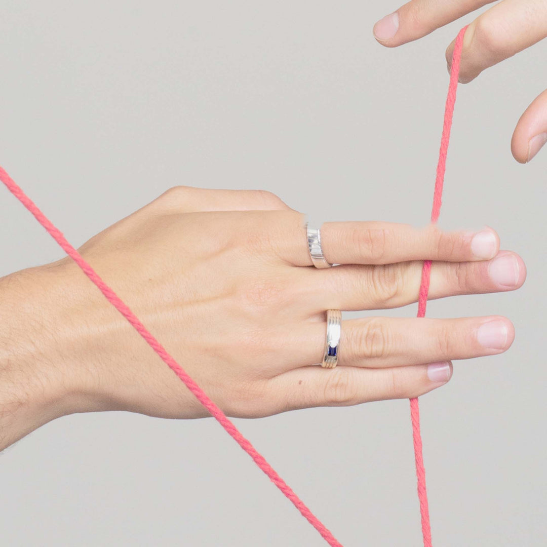 mans hand wearing two white gold mens engagement rings and holding onto red string