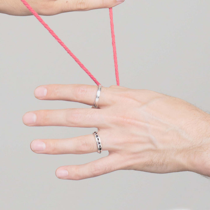 single hand holding a red string wearing two solid white gold mens engagement rings