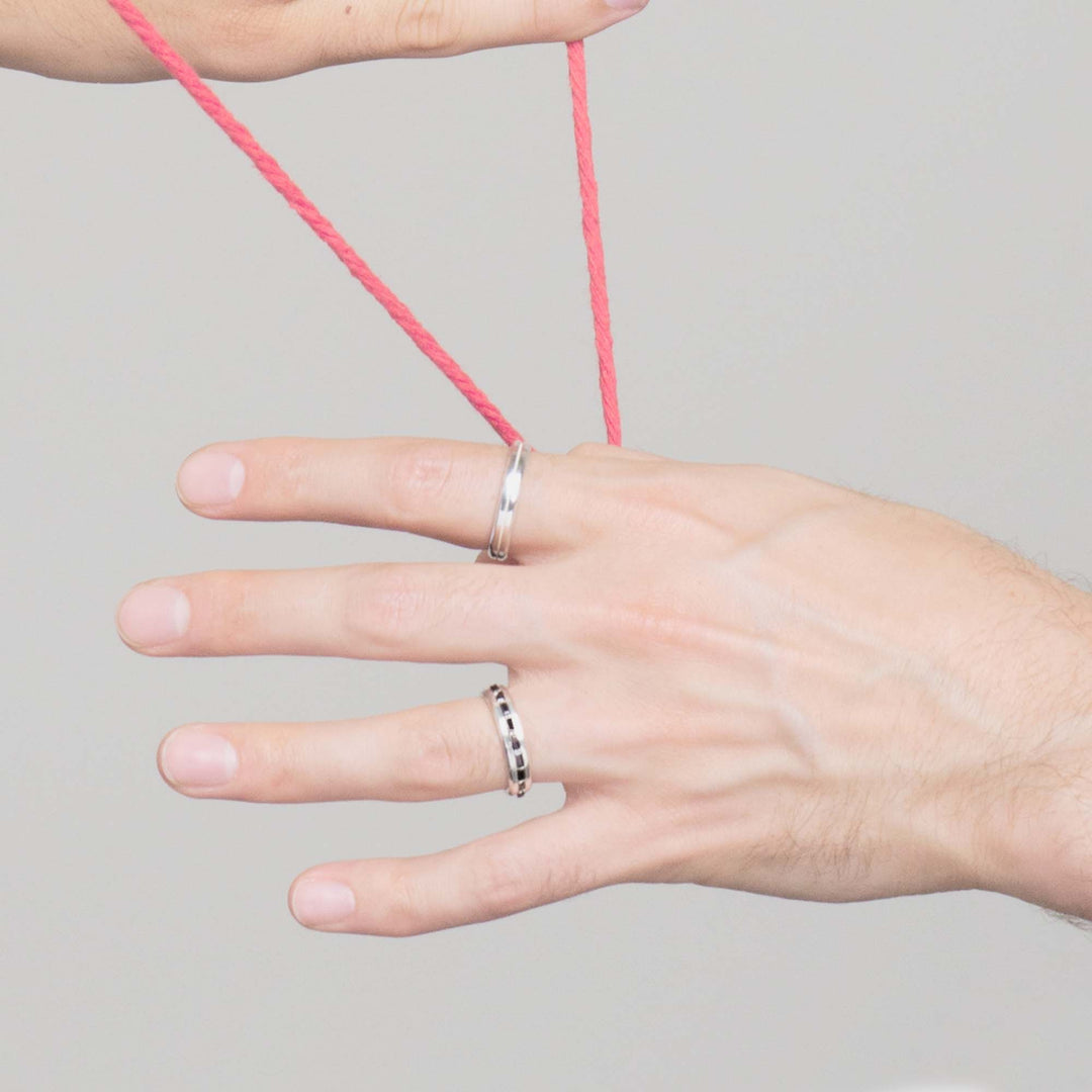 single hand holding a red string wearing two solid white gold mens engagement rings