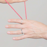 single hand holding a red string wearing two solid white gold mens engagement rings