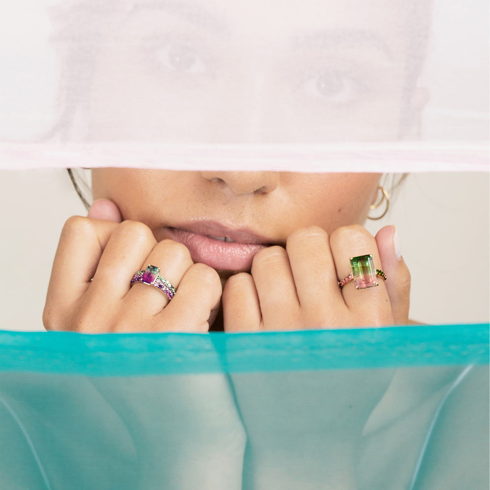 close up of woman wearing two watermelon tourmaline cocktail rings with fists held beneath chin. Two pieces of fabric divide scene from top and bottom