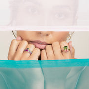 close up of woman wearing two watermelon tourmaline cocktail rings with fists held beneath chin. Two pieces of fabric divide scene from top and bottom