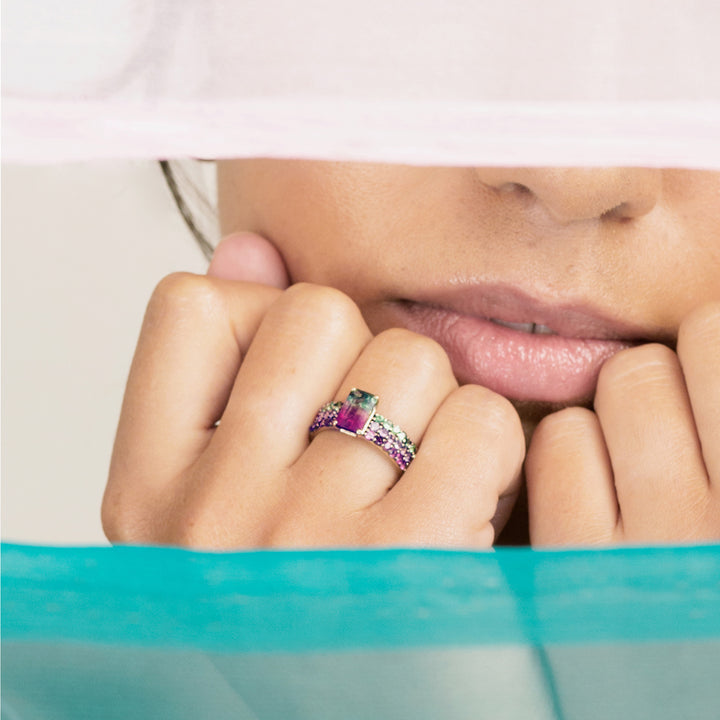 close up of a woman wearing a yellow gold wide band watermelon tourmaline ring on clenched fist under her lips